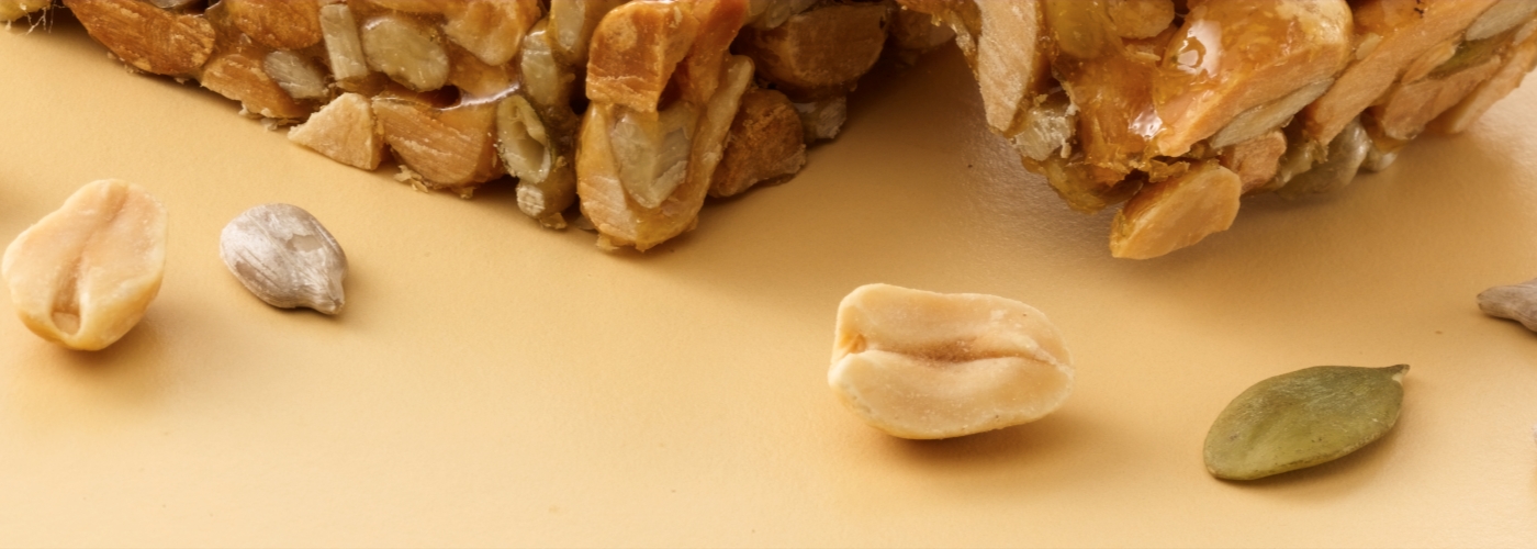Assorted nuts and seeds scattered on a beige surface: peanuts, cashews, hazelnuts, and pumpkin seeds