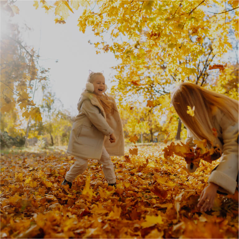 little girl and mother playing with orange and yellow crispy autumn leaves