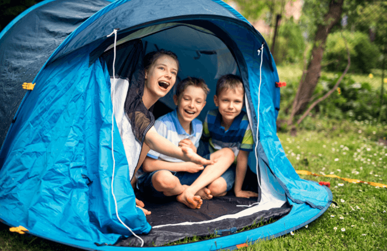 Kids enjoying backyard camping in a blue tent.