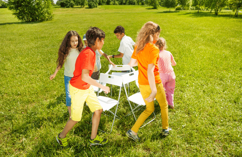 A group of 6 kids playing musical chair in a garden.