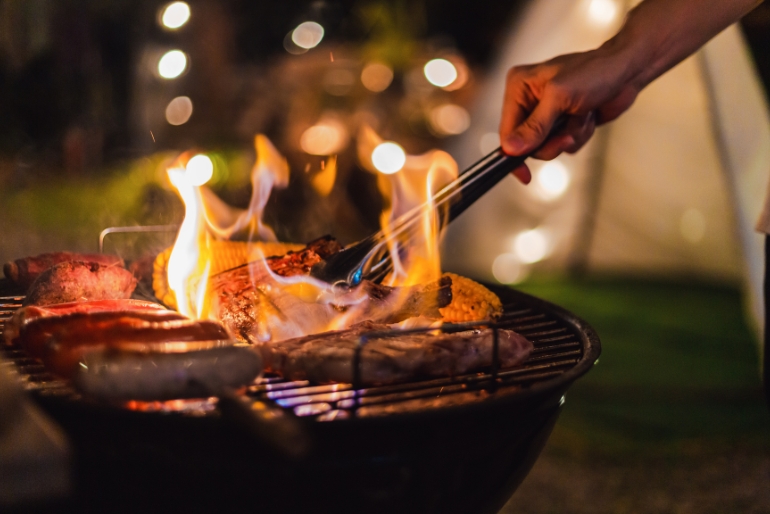 A man cooking on a Barbeque in the night on a campsite.